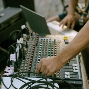 A close-up of a hand adjusting an audio mixer in a studio, showcasing cables and sound equipment.